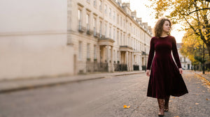 Woman in a burgundy velvet long sleeve midi dress walking down a city street in autumn